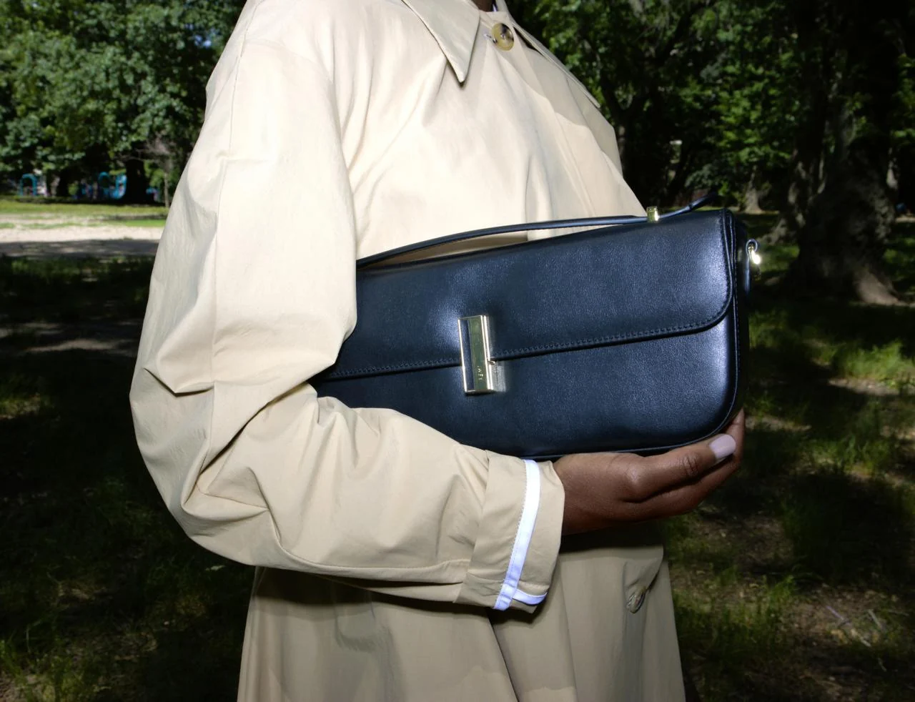 Model in an ivory coat holding a navy leather handbag